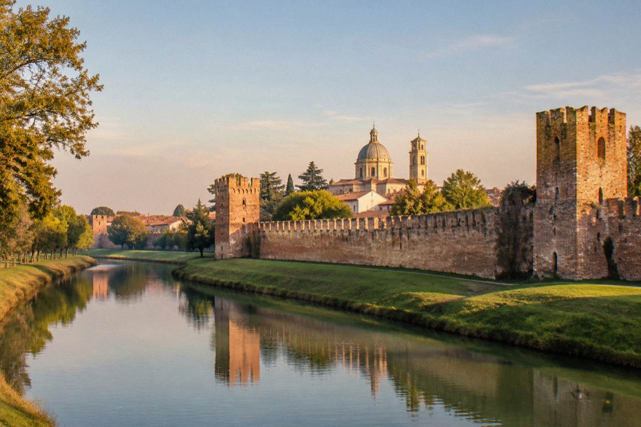Red brick medieval town walls surrounding Castelfranco Veneto with a grassy moat and trees