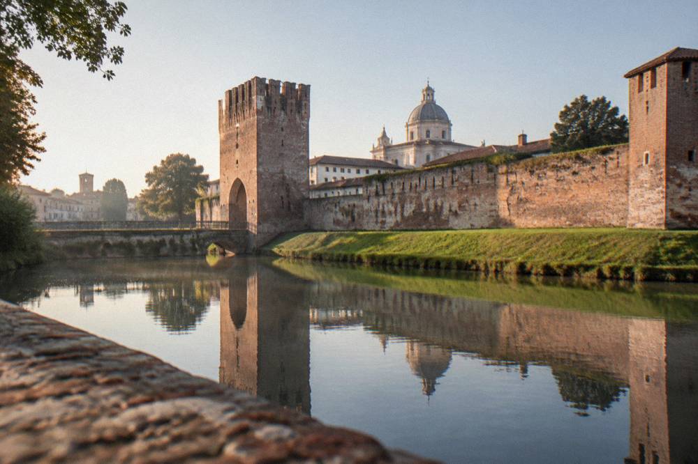 Reflected brick wall and gate of Castelfranco Veneto seen across the water of the moat