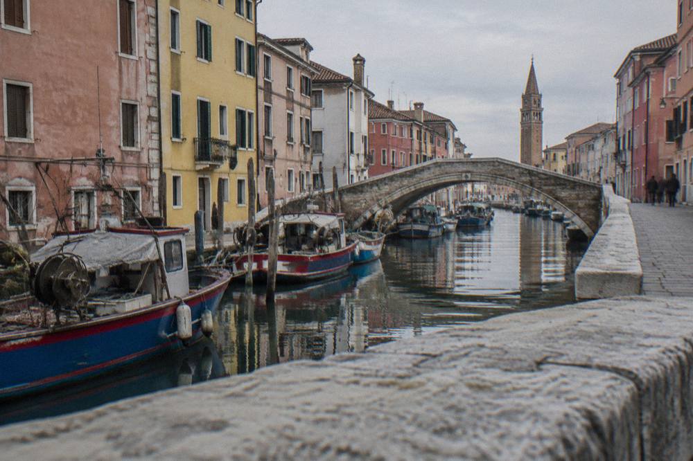 A stone bridge crossing a narrow canal between tall painted houses in Chioggia