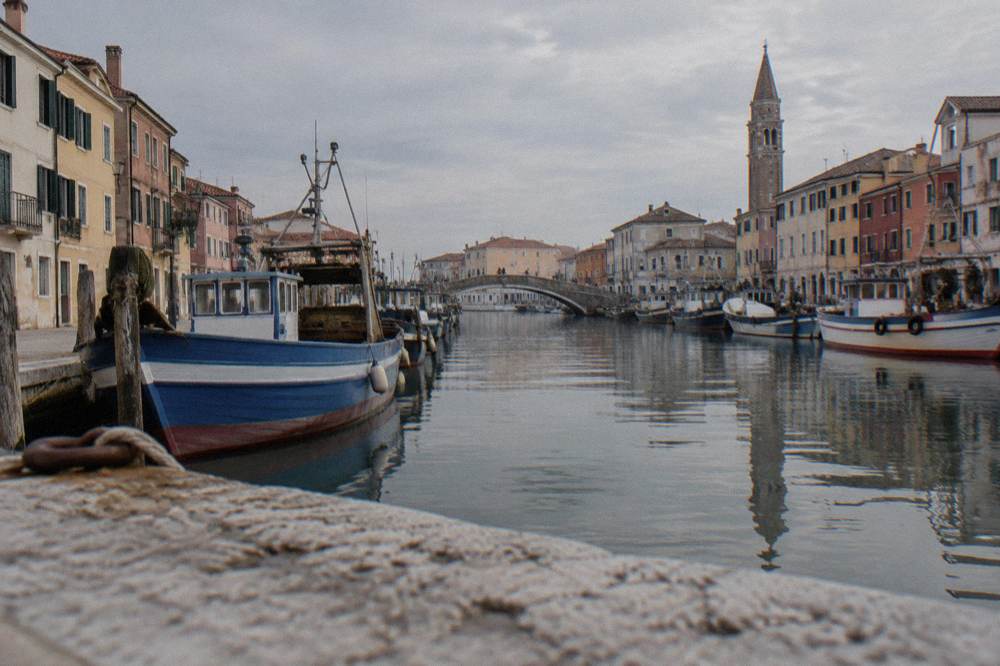 A wide canal lined with boats and buildings leading toward a bridge in Chioggia