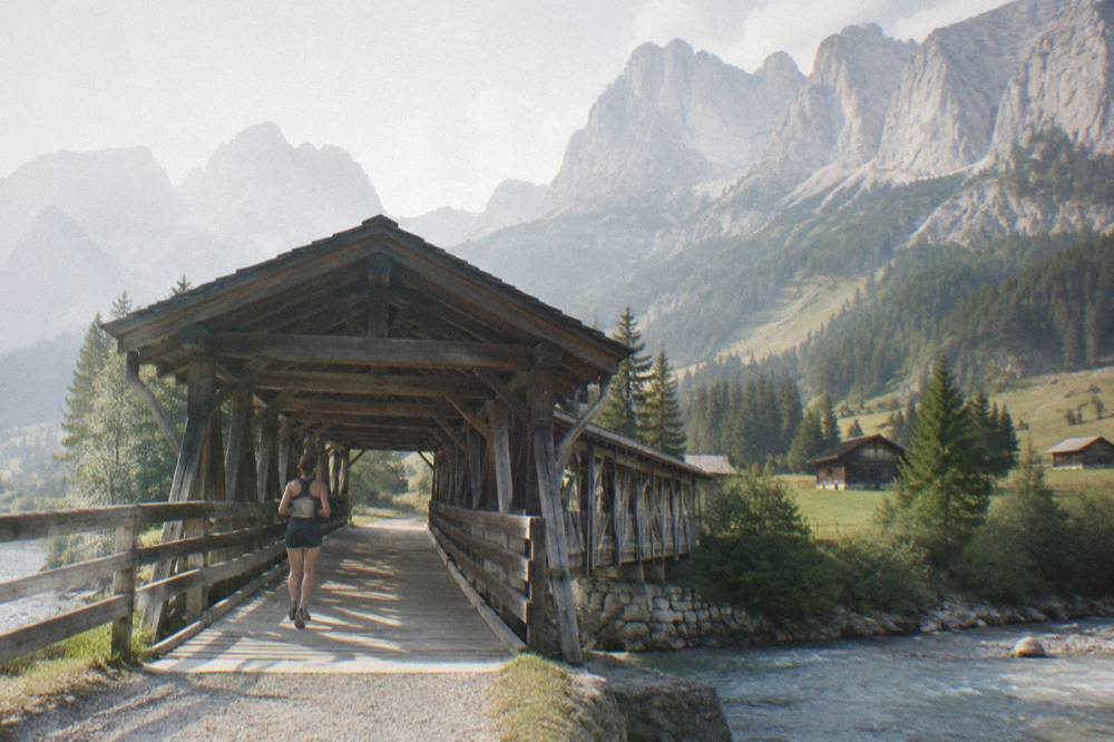 A covered wooden alpine bridge over a river with mountains in the background