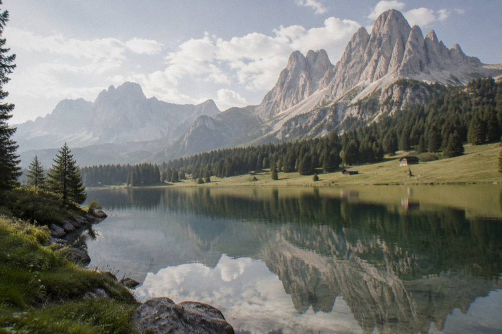 An alpine lake reflecting jagged pale mountain peaks under scattered clouds