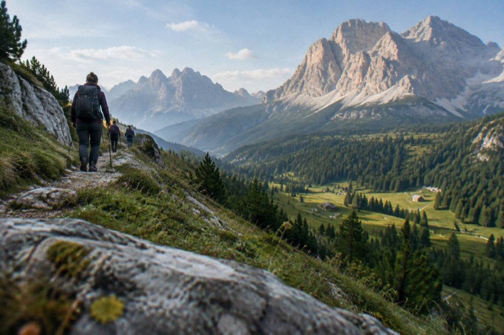 Hikers on a mountain trail above a valley with layered rock peaks in morning light
