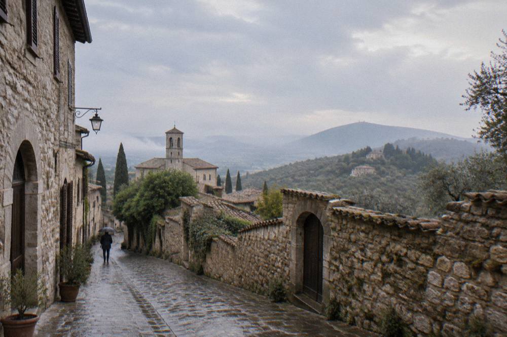 A stone village street with arched doorways climbing a wooded hillside