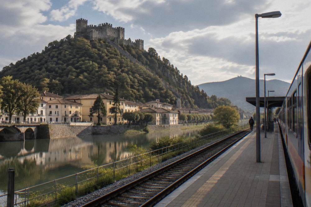 A regional train at an Italian station platform with hills in the background