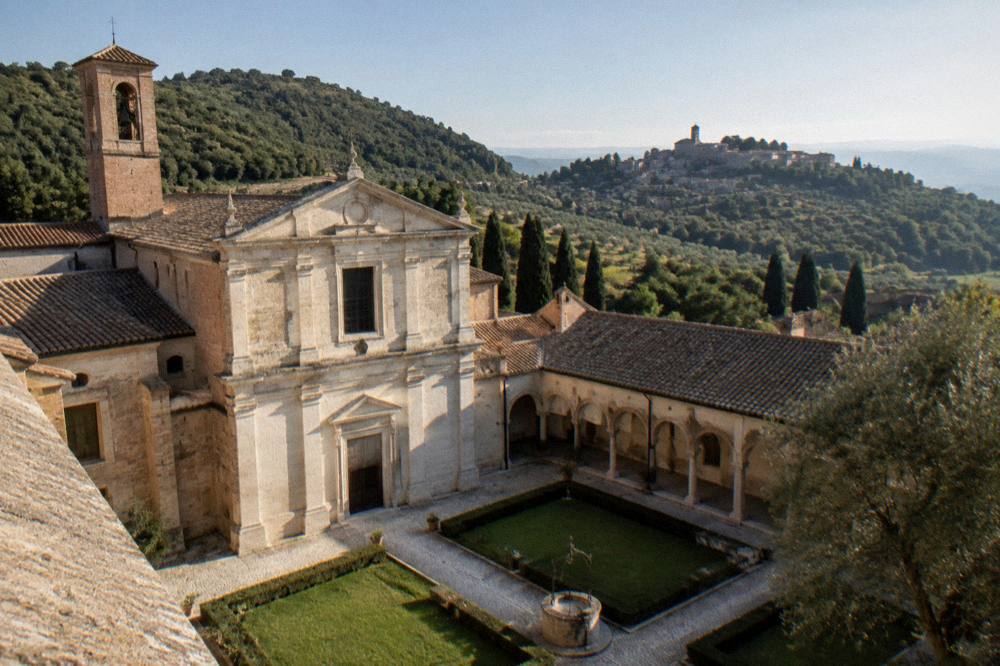 A walled hill town seen across olive groves and cypress trees