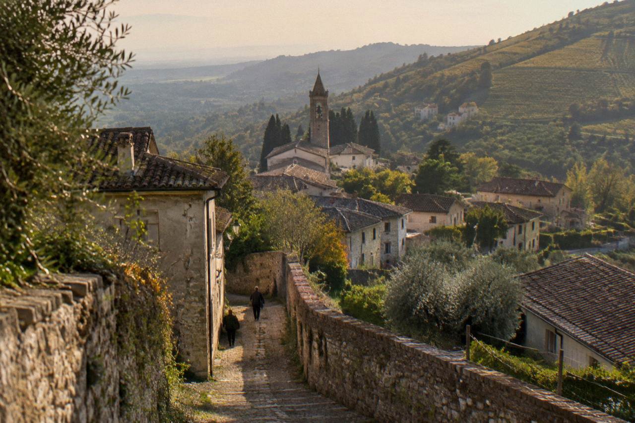 Steep vineyard-covered hillsides rising in rows above a small village in the Veneto countryside