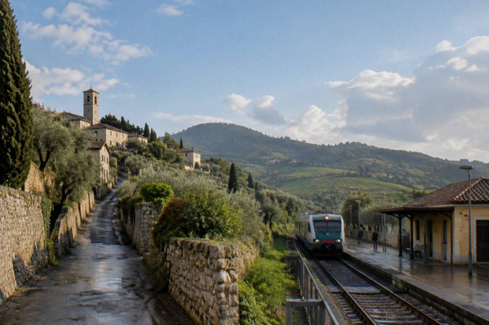 A regional train pulling into a small station beneath hills covered in vineyards