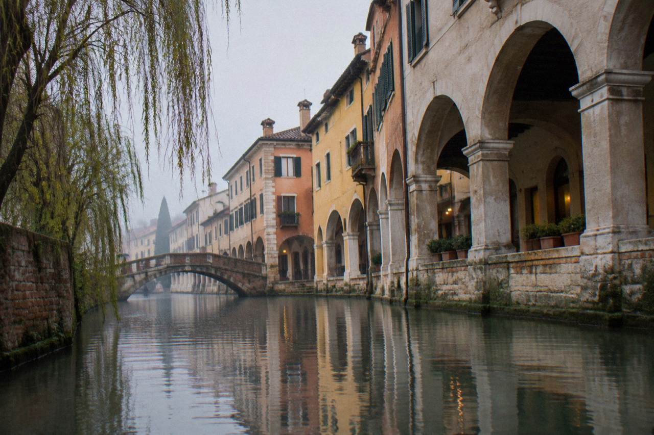 A quiet canal in Treviso with a stone bridge and arcaded buildings along the water