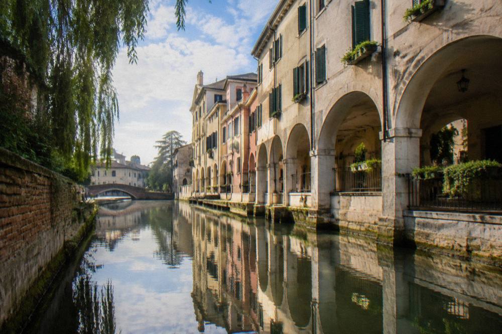 Arcaded houses in Treviso reflected in a narrow canal under a bright sky