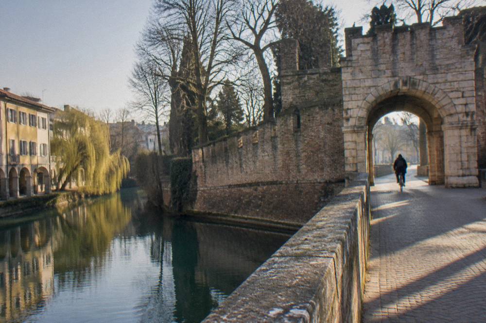 A stone gate in Treviso's city walls with trees and a cyclist passing through