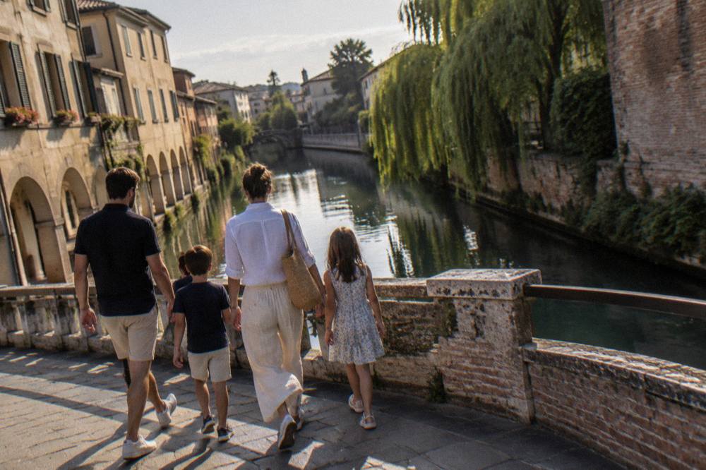 A family walking across a small bridge over a Treviso canal in late afternoon light