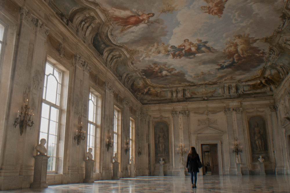 Looking up at a painted ceiling with figures and clouds in a grand hall