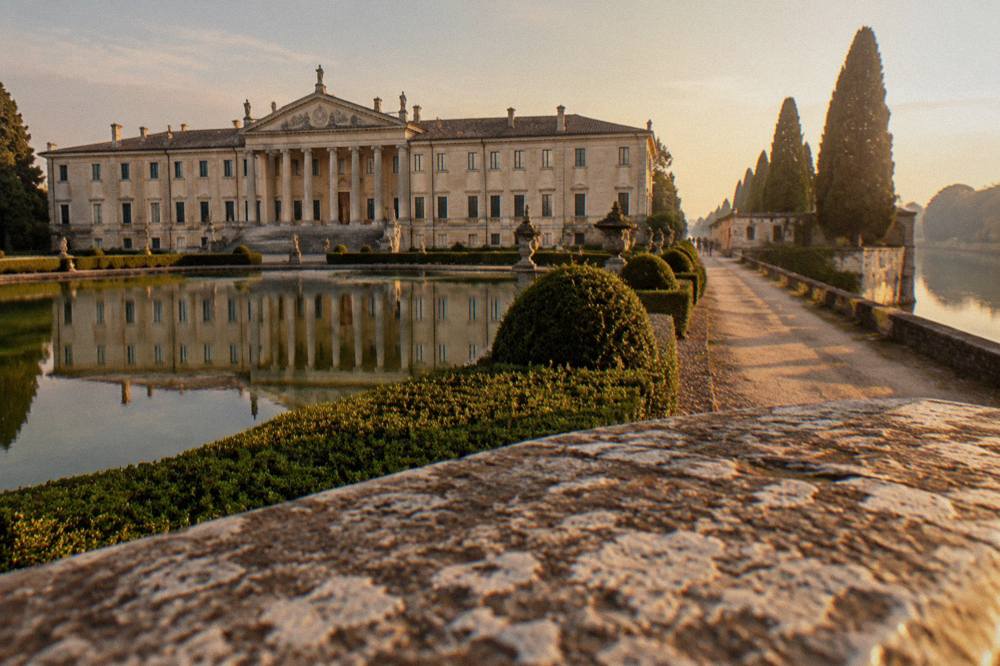 A riverside path along a canal with cypress trees and a villa wall