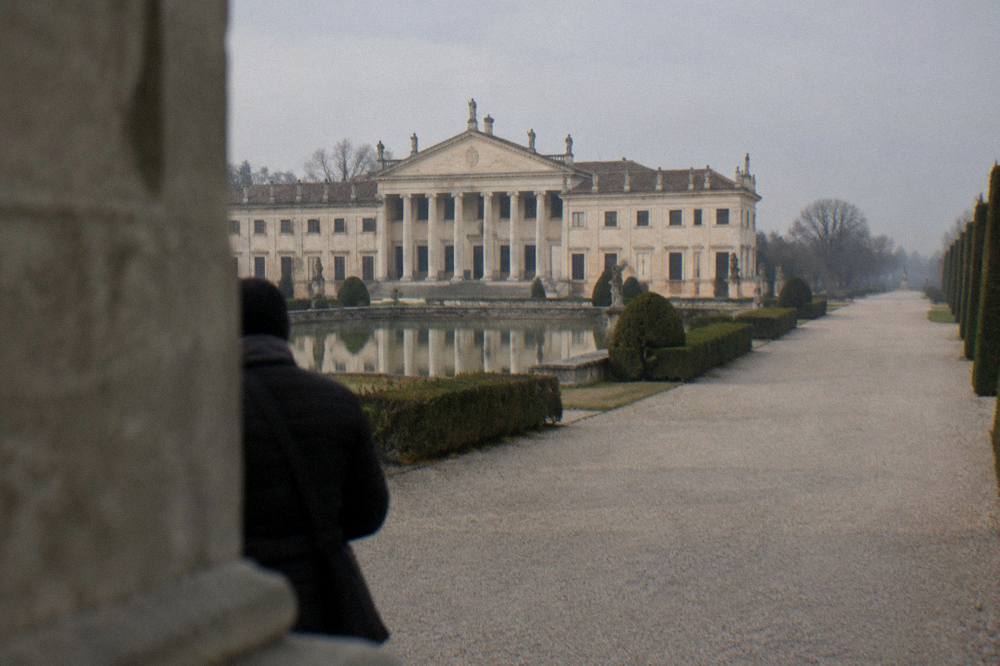 Wide gravel avenue in a villa park with clipped hedges and distant statuary