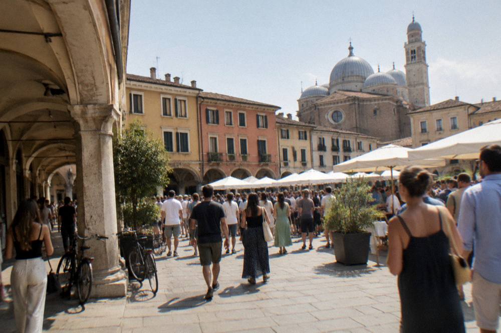 Crowds gathered in a Padua square during a festival with banners in daylight