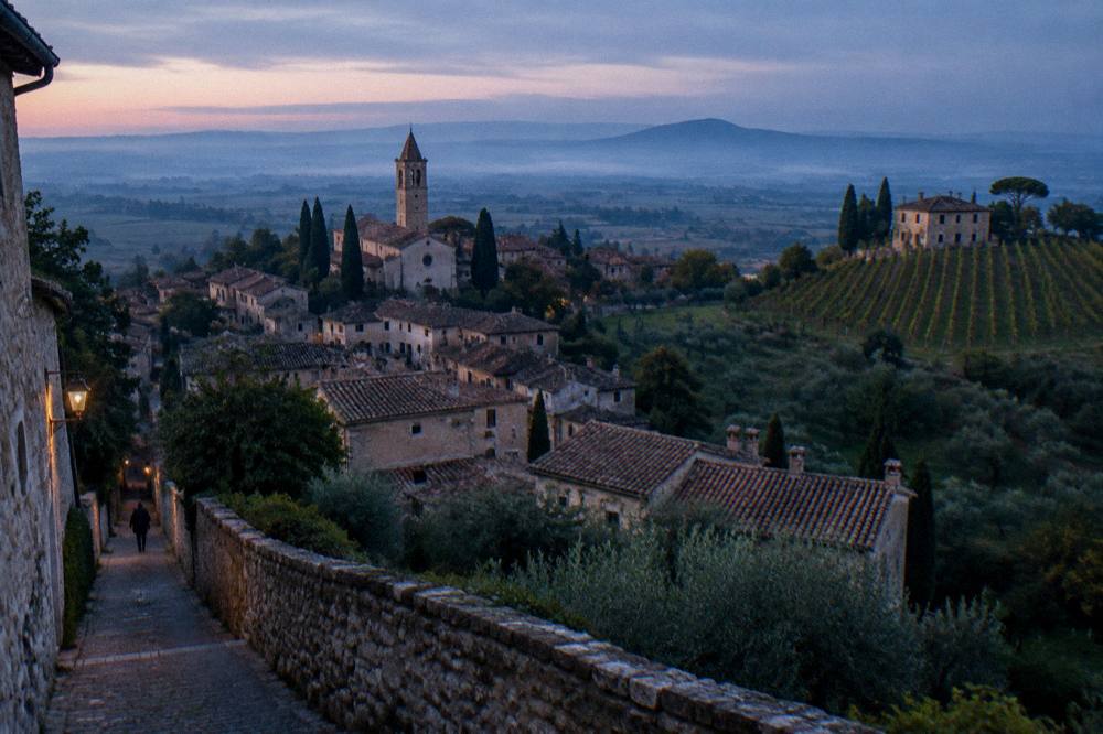 A vineyard slope with a stone farmhouse and cypress trees above a misty plain