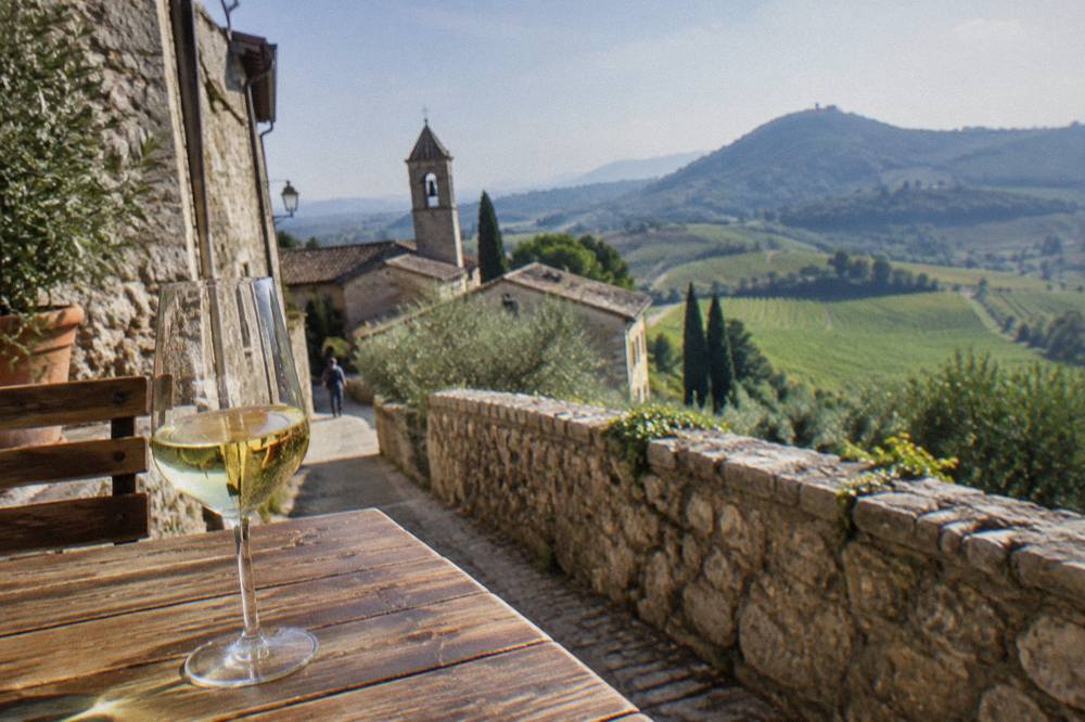 A glass of white wine on a wooden table overlooking rolling vineyards