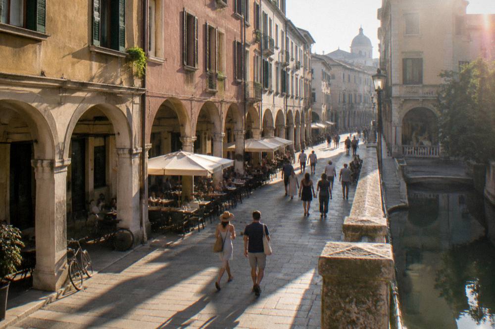 An arcaded street in central Padua with cafe tables and people walking on a June afternoon