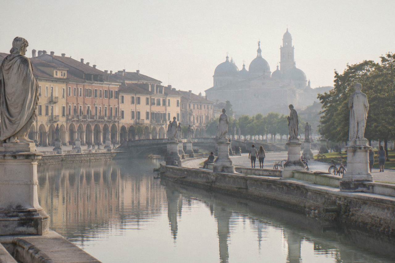 A wide canal-ringed square in Padua with rows of statues and people walking