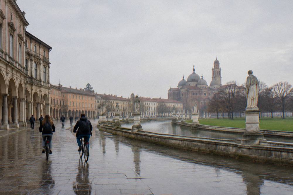 Students cycling past an arcaded street and old palace in a university city
