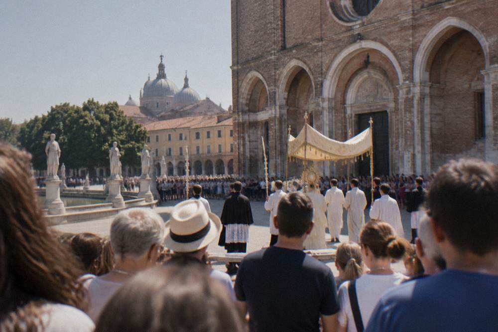 A crowd watching a procession pass a large brick church in an Italian square