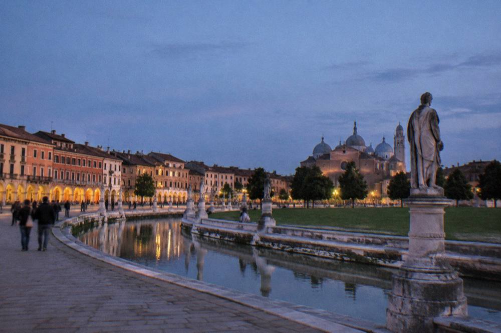 People strolling at dusk under lit arcades in an Italian square