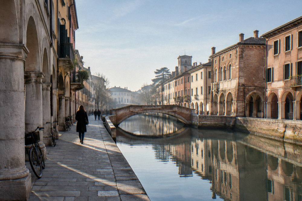 A canal in Padua reflecting old brick facades and a small bridge