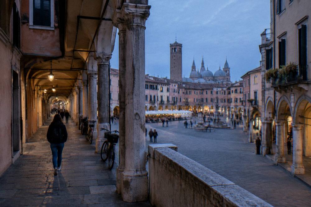 A visitor with a backpack walking under the porticoes toward Piazza delle Erbe