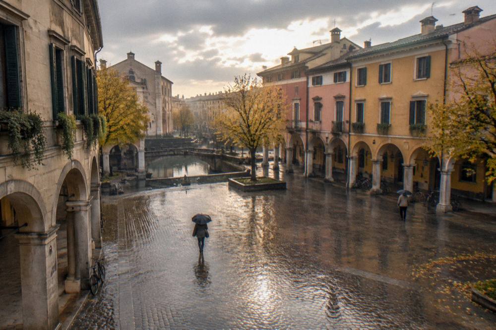 Rain falling on an empty Padua square with wet cobblestones reflecting the arcades