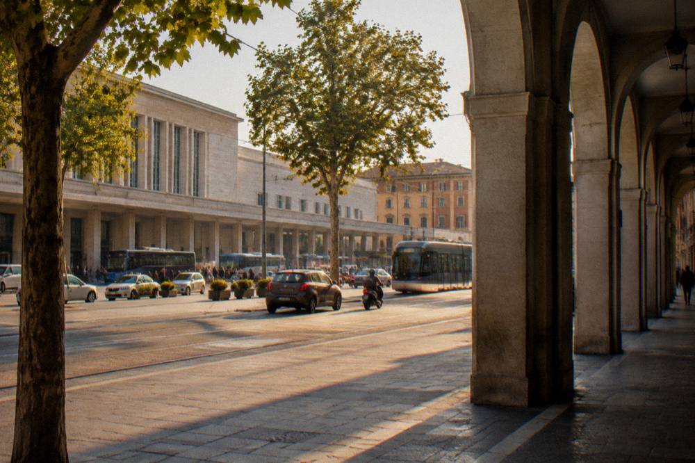 Cars and scooters moving through a narrow arcaded street in an Italian city centre