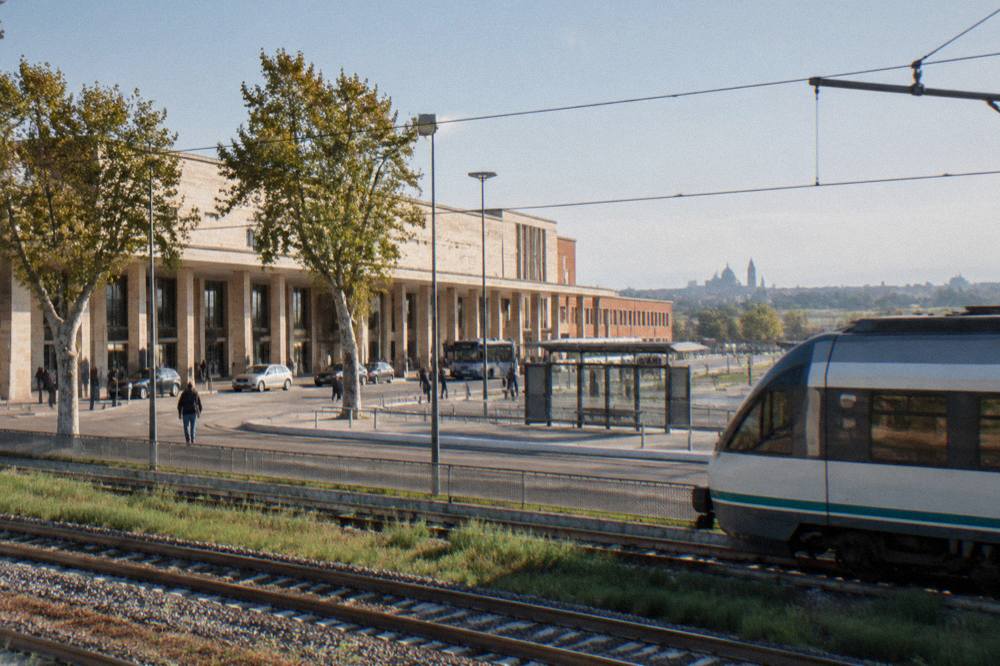A regional train crossing flat countryside with a distant city skyline