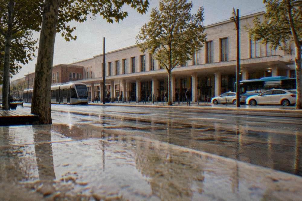 Wide city avenue with trees and low buildings near a railway station