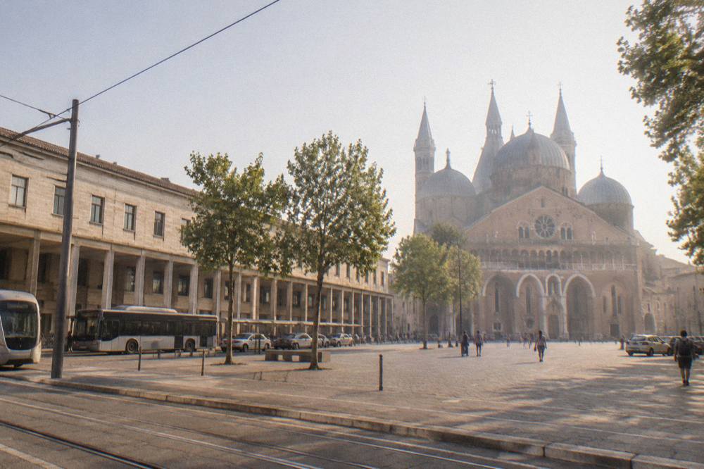 Sunlight on the facade of a large basilica with domes and a wide paved square