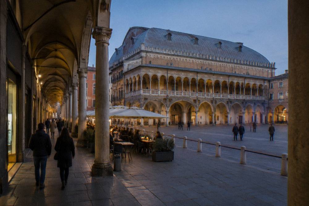 Visitors walking through an arcaded street in Padua's old centre past café tables and shopfronts