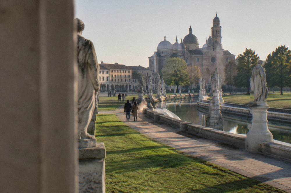 Visitors walking across Prato della Valle square with its canal and statues