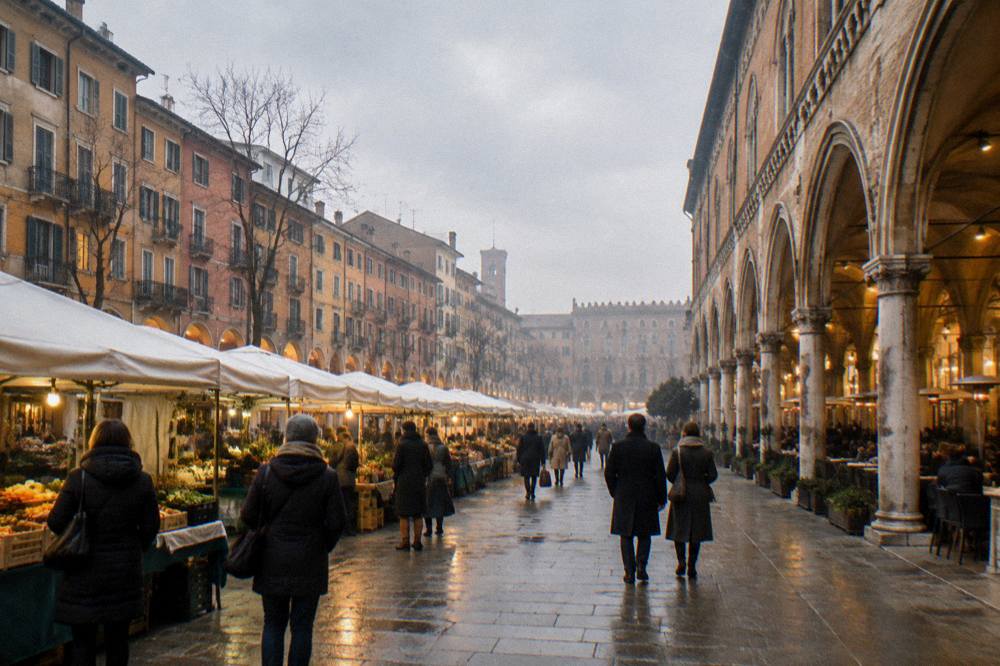 An evening piazza with lit cafés under arcades and people walking with coats and scarves