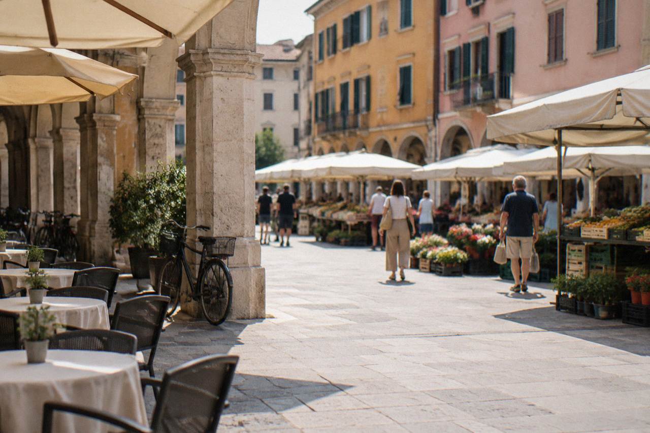 Market stalls and café tables under the arcades of a Padua square on a bright morning