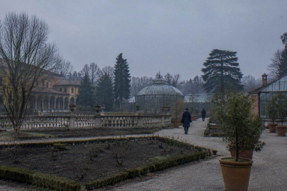 Bare garden beds and evergreen structures inside the Orto Botanico on a grey day