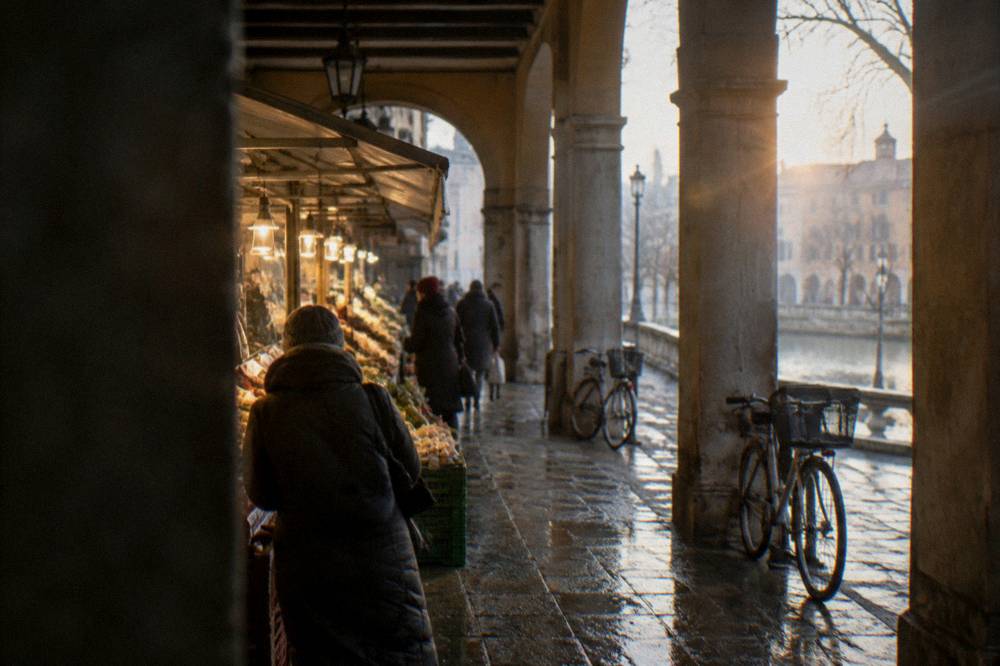 A covered market hall in Padua with food stalls lit against a wet afternoon outside