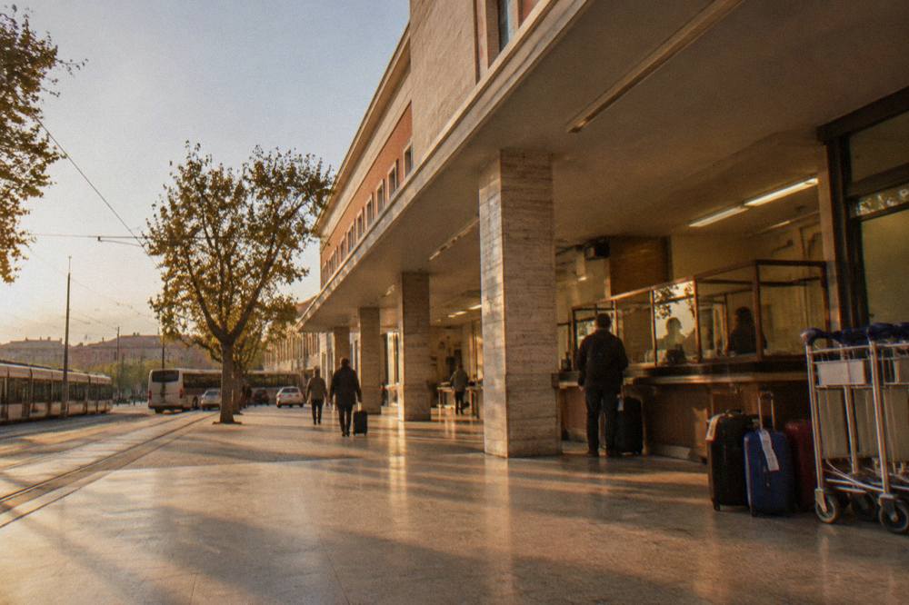 A staffed left-luggage counter beside a railway platform with trolleys and tagged suitcases