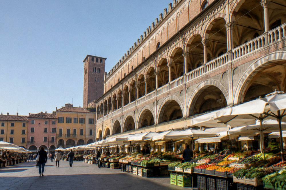 An arcaded market square in Padua with stalls and historic buildings under morning light