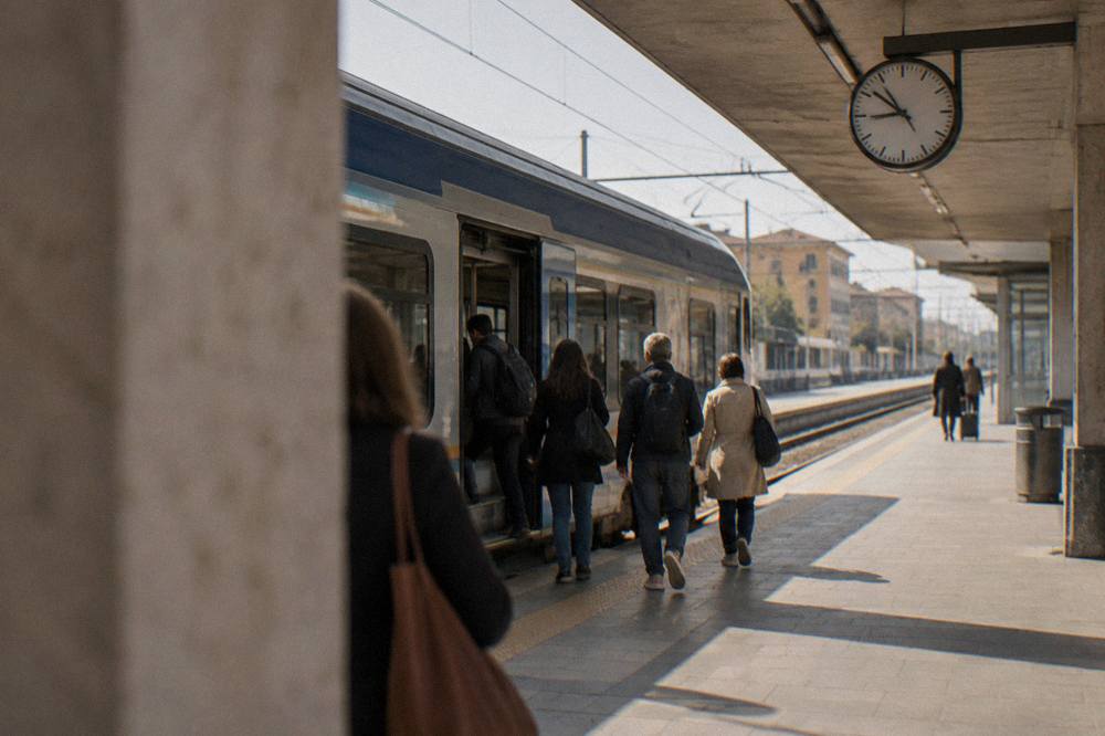 A regional train at a platform with passengers boarding and a clock above the tracks