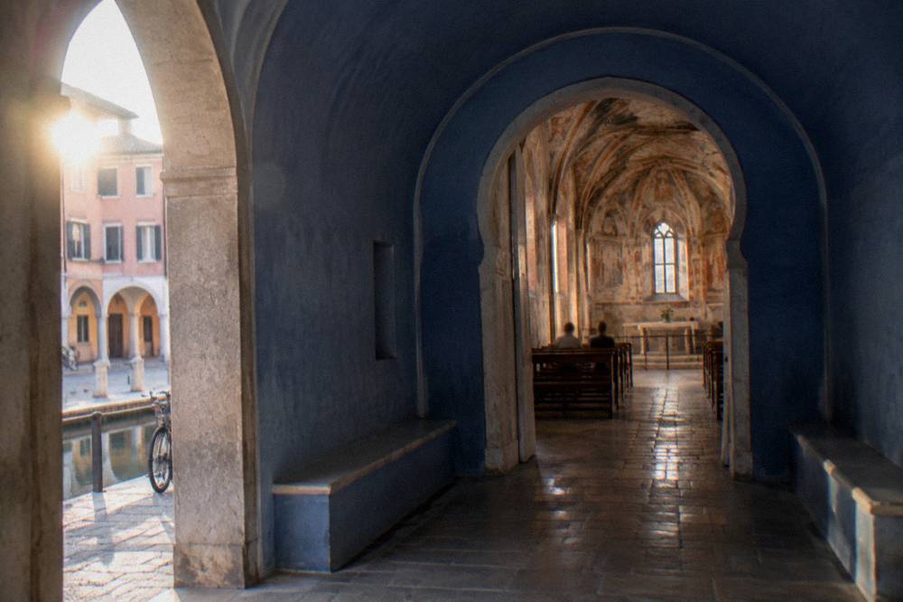 Blue horseshoe-shaped queue room leading into a frescoed medieval chapel interior