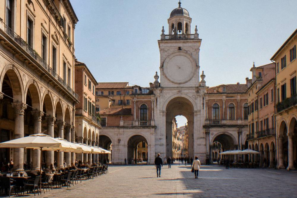Cobblestones square with cafe tables under arcades and a medieval clock tower above