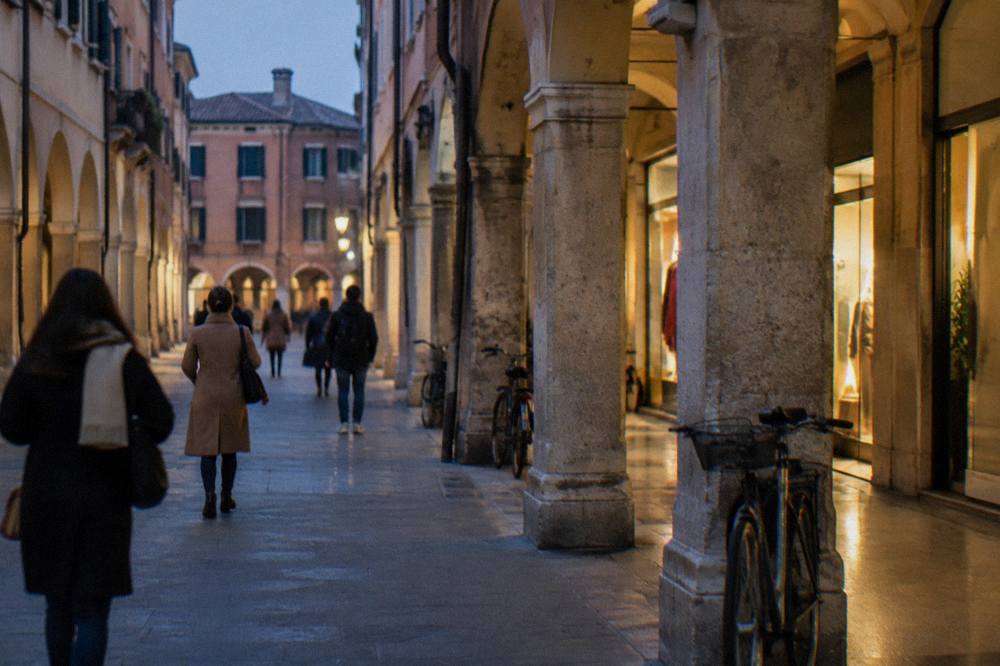 People walking through a narrow arcaded shopping street in central Padua