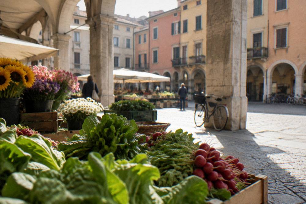 Market stalls with vegetables and flowers in a Padua square under arcades