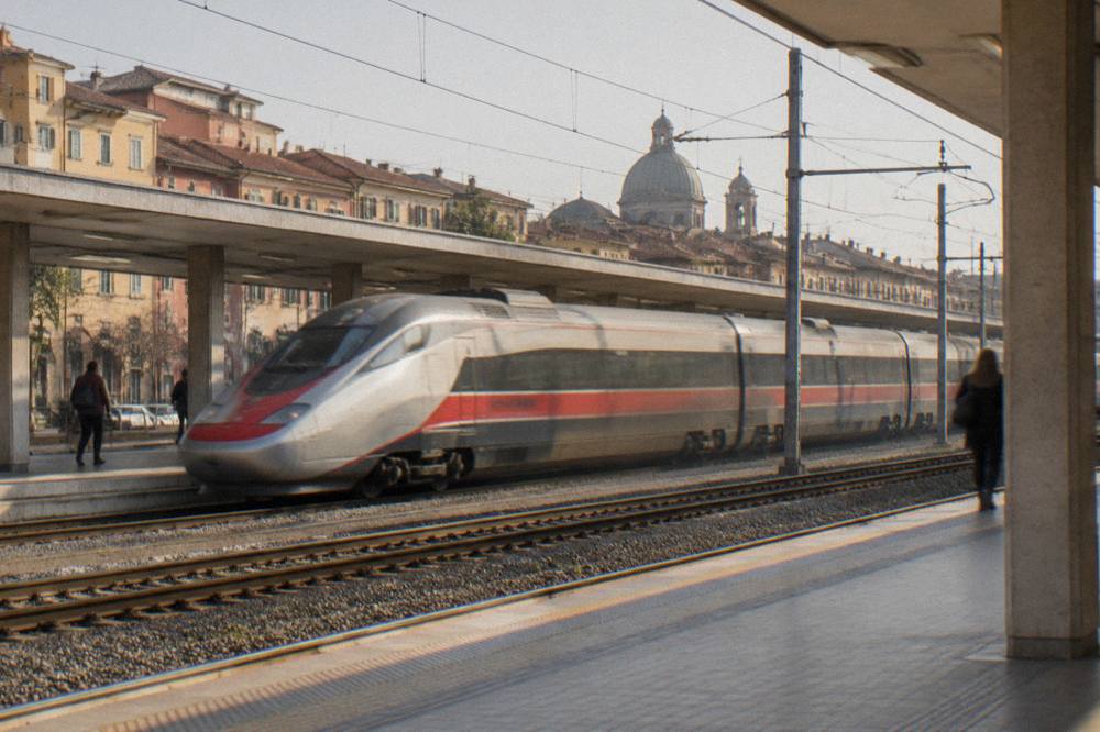 A high-speed train passing through Padua station platforms in the late afternoon
