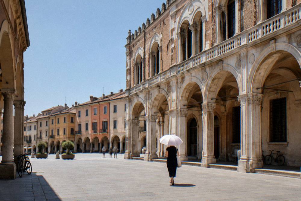 Person with umbrella walking past a Renaissance palace facade in Padua