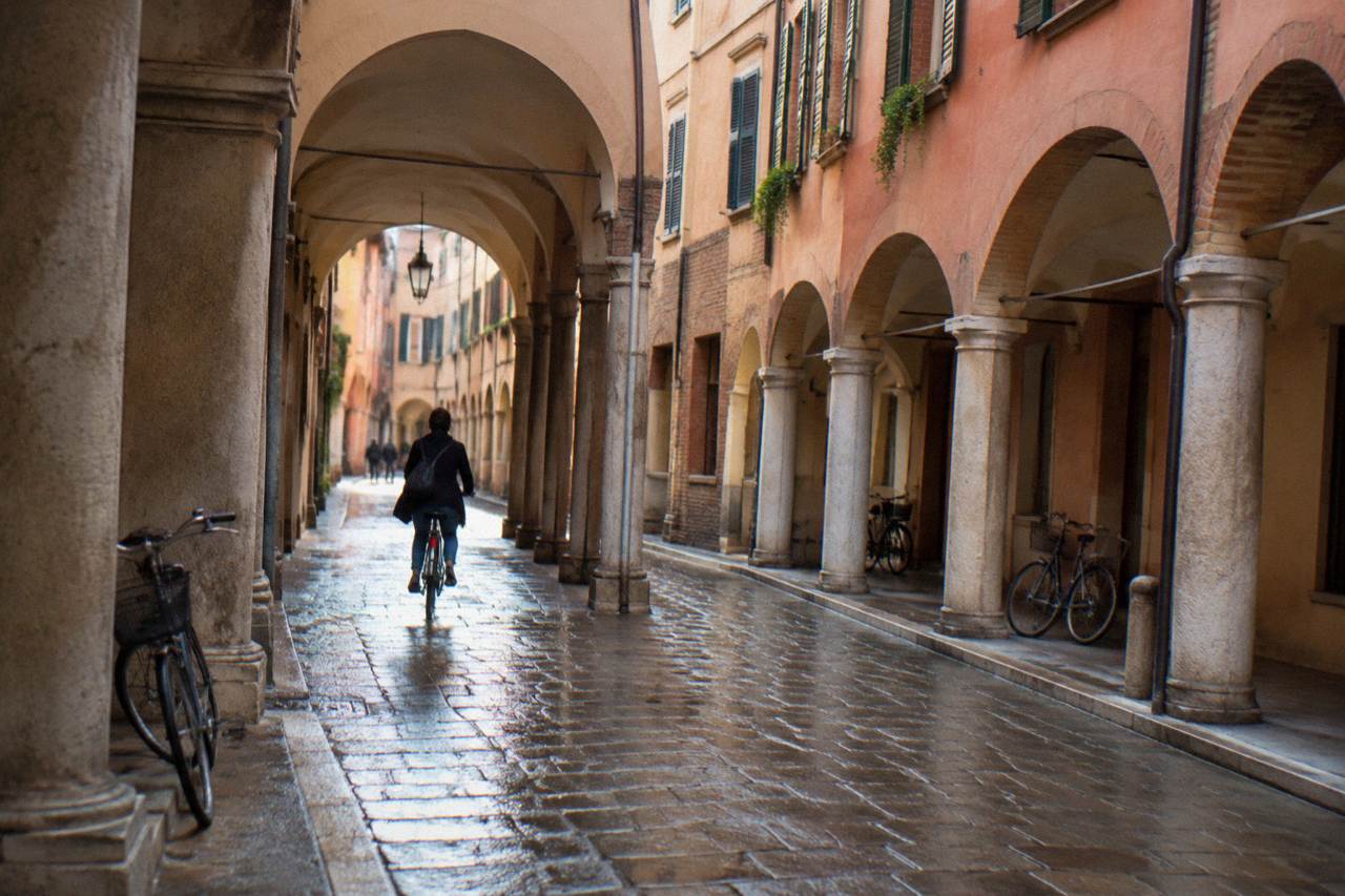 A narrow arcaded street in Padua's historic centre with a cyclist passing under the medieval arches
